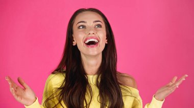 amazed young adult woman with outstretched hands isolated on pink