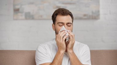 man with pollen allergy sneezing in napkin at home