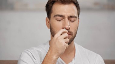 allergic man using nasal spray at home 