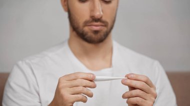 cropped view of blurred man holding electronic thermometer at home