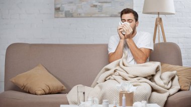 diseased man drinking tea while sitting on couch 