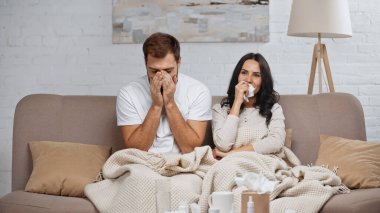 sick couple sneezing and coughing in living room 