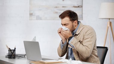 allergic businessman sneezing in napkin near laptop on desk 