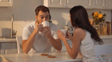 bearded man drinking coffee and looking at blurred girlfriend 