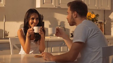 joyful woman holding cup of coffee and smiling near blurred boyfriend 