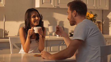 joyful young woman holding cup and smiling near blurred boyfriend 