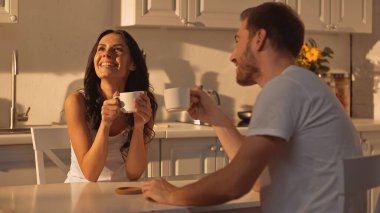 cheerful young woman holding cup and smiling near boyfriend 