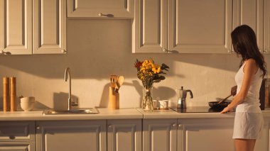 brunette young woman in pajamas cooking in modern kitchen 