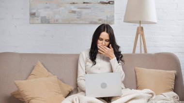 sick brunette freelancer with running nose using laptop in living room 