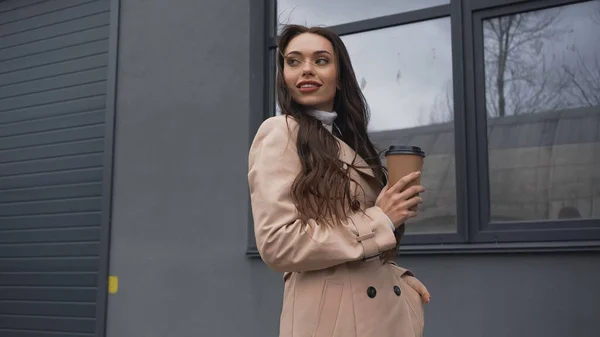 Smiling Young Adult Woman Trench Coat Holding Paper Cup Building — Φωτογραφία Αρχείου