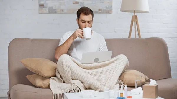 Sick Man Sitting Sofa Laptop Drinking Tea Coffee Table Pills — 图库照片