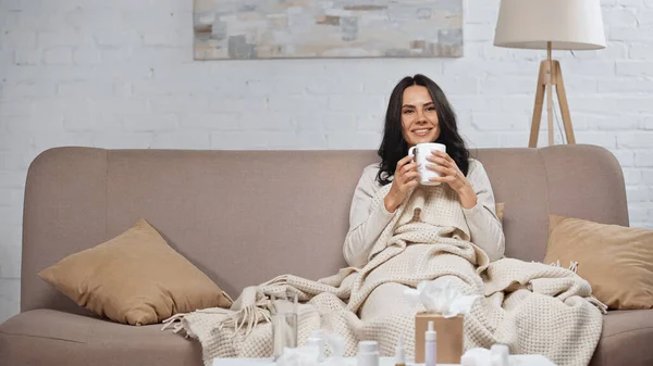 Sick Brunette Woman Holding Cup Tea Smiling While Sitting Couch — Fotografia de Stock