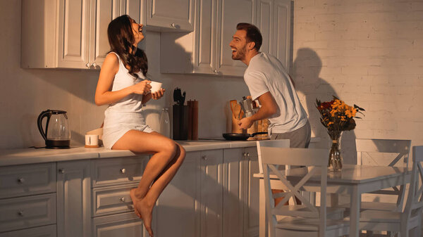 счастливая женщина сидит на кухне шкаф с чашкой и смеется с парнем 