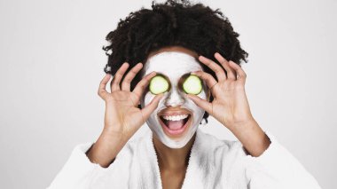 Heyecanlı Afro-Amerikan kadın maske takıyor. Elinde salatalık dilimleri var. 
