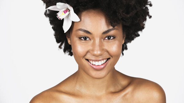 Pretty african american woman with white orchid in hair smiling at camera isolated on grey 