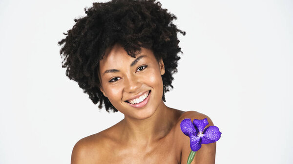 Smiling african american woman with clean skin holding orchid isolated on grey 