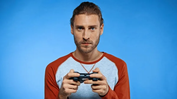 KYIV, UKRAINE - NOVEMBER 24, 2020: bearded man holding joystick while playing video game on blue — Stock Photo