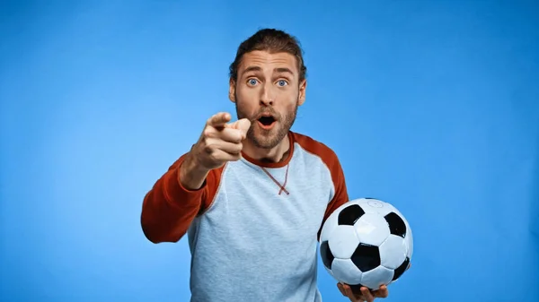 Удивленный футбольный болельщик держит мяч и указывает пальцем на синий — стоковое фото