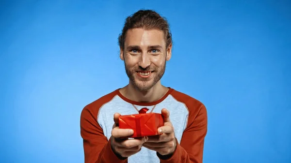 Happy bearded man holding wrapped present on blue — Stock Photo