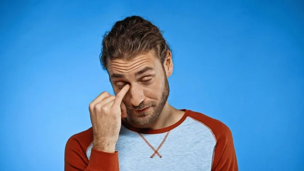 Tired man rubbing eye with finger on blue — Stock Photo