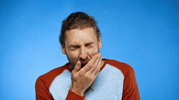 Tired man yawning and covering mouth on blue — Stock Photo