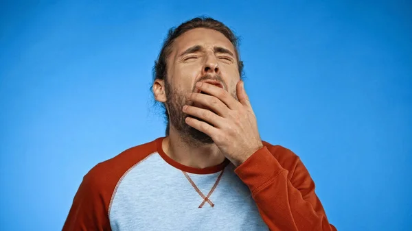 Hombre somnoliento con los ojos cerrados bostezando y cubriendo la boca en azul - foto de stock