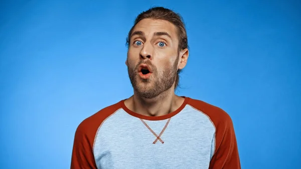 Hombre sorprendido y barbudo con la boca abierta mirando a la cámara en azul - foto de stock