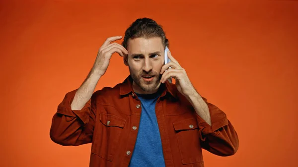 Confused young man talking on smartphone on orange — Stock Photo