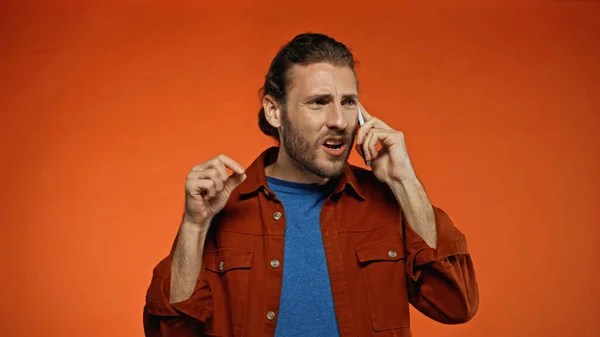 Displeased young man talking on mobile phone on orange — Stock Photo