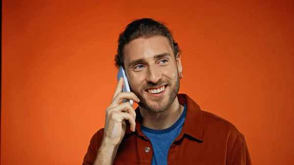 Happy young man talking on mobile phone on orange — Stock Photo