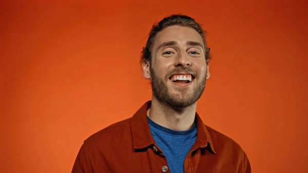 Homme joyeux et barbu souriant tout en regardant la caméra sur orange — Photo de stock