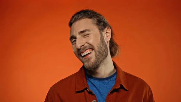 Joyful and bearded man winking eye while looking at camera on orange — Stock Photo