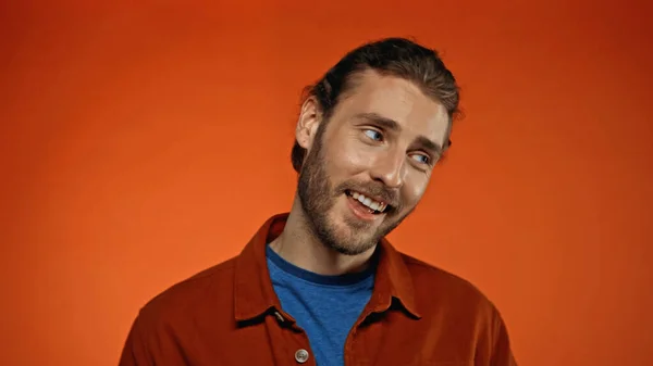 Joyful and bearded man smiling while looking away on orange — Stock Photo