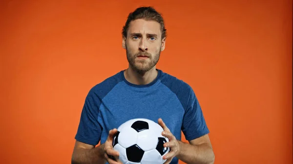 Abanico de fútbol en camiseta azul sosteniendo pelota de fútbol en naranja - foto de stock
