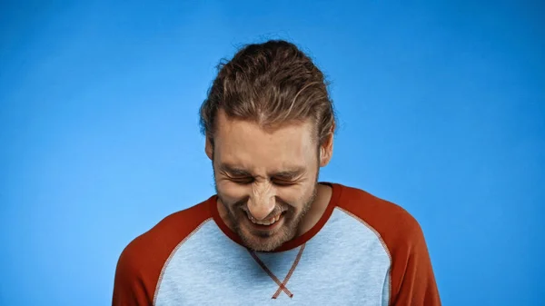 Bearded young man with closed eyes laughing on blue — Stock Photo