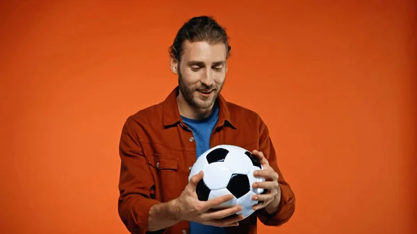 Happy football fan looking at soccer ball on orange — Stock Photo