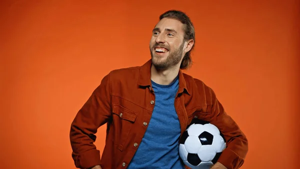 Счастливый футбольный болельщик смотрит в сторону и держит футбольный мяч на апельсине — стоковое фото