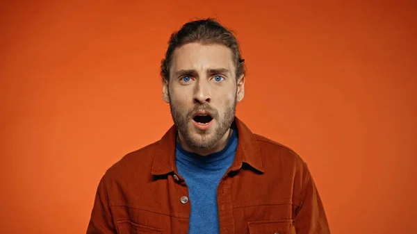 Shocked young man with open mouth looking at camera on orange — Stock Photo