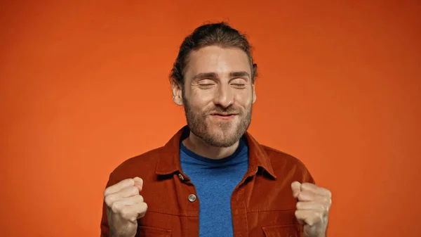 Excited man with closed eyes and clenched fists on orange — Stock Photo