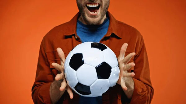 Обрізаний вид збудженого чоловіка, що тримає футбольний м'яч на помаранчевому — стокове фото