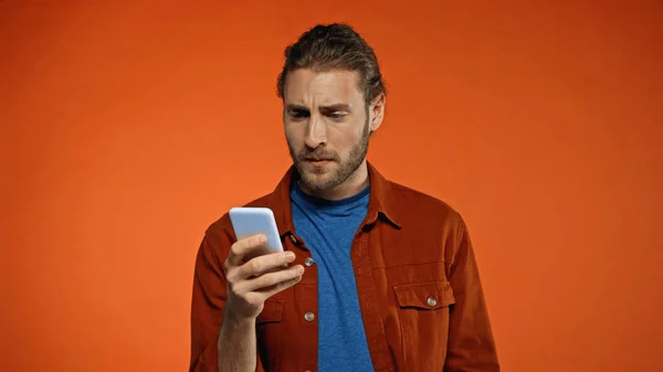 Homme barbu concentré en utilisant le téléphone mobile sur fond orange — Photo de stock