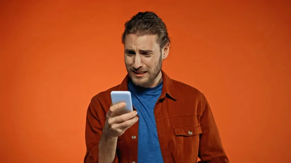 Triste joven usando el teléfono móvil en naranja - foto de stock