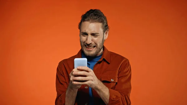 Jovem frustrado usando telefone celular em laranja — Fotografia de Stock