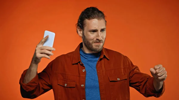 Jeune homme mécontent tenant téléphone portable sur orange — Photo de stock