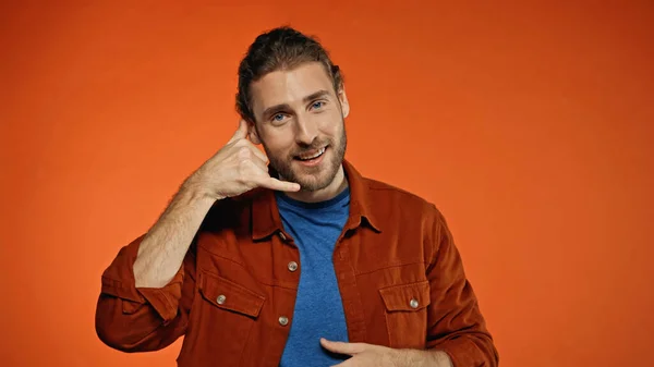 Positive young man showing call me gesture on orange — Stock Photo