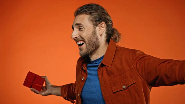 Heureux jeune homme souriant tout en tenant enveloppé présent sur orange — Photo de stock