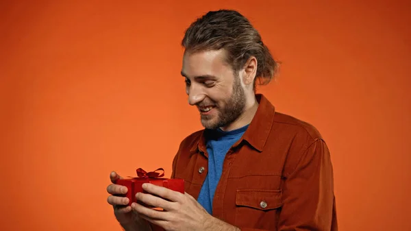 Joven feliz mirando regalo envuelto en naranja - foto de stock