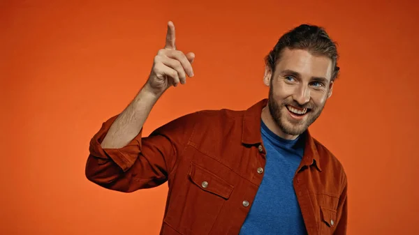 Joven positivo y hombre barbudo sonriendo mientras señala con el dedo en naranja - foto de stock