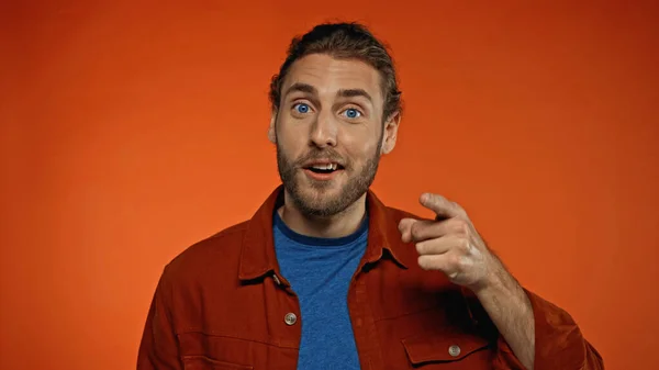 Young bearded man pointing with finger while looking at camera on orange — Stock Photo