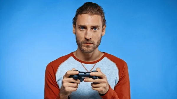 QUIIV, UCRÂNIA - NOVEMBRO 24, 2020: jovem segurando joystick enquanto joga videogame em azul — Fotografia de Stock